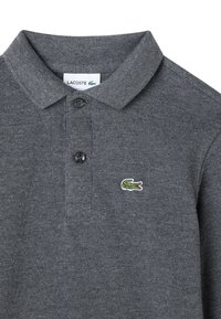 Polo shirt grigio scuro con due bottoni neri e logo del coccodrillo verde Lacoste sul lato sinistro del petto.