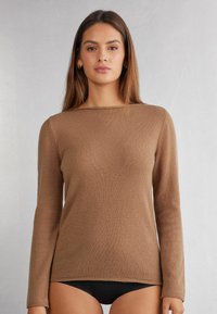 Brauner Langarmpullover mit geripptem Muster, Rundhalsausschnitt und lockerer Passform, kombiniert mit schwarzen Hosen. Schlichtes und unauffälliges Design.