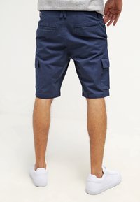 Shorts cargo marine en coton, avec poches latérales, une coupe droite et des coutures visibles. Associés à des baskets blanches.