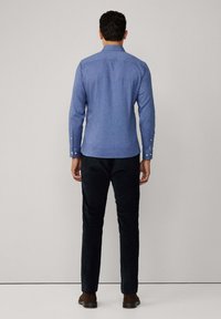 Chemise bleu clair à manches longues avec un col boutonné et des poignets boutonnés, assortie à un pantalon noir et des chaussures marron.