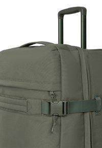 Sac de voyage à roulettes vert olive avec poignée robuste, fermeture latérale à boucle et tissu texturé. Comprend plusieurs poches de rangement.