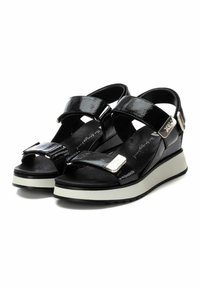 Sandalias de charol negro con dos correas ajustables, una plantilla texturizada y una suela de plataforma blanca de contraste. Presentan detalles en plata.