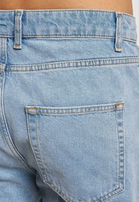 Jeans de mezclilla azul claro con un bolsillo trasero con costura visible. La tela tiene una textura ligeramente desgastada y un corte clásico.