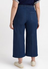 Breda denimbyxor i mörkblått med elastisk midja och en enda bakficka. Slät textur och rak nederkant vid anklarna.