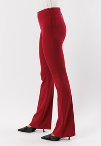 Pantaloni aderenti rossi con vita alta e chiusura con zip. Tessuto liscio con una leggera lucentezza, design a gamba svasata, scarpe nere a punta a contrasto.