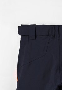 Navyblauwe broeken met een brede tailleband en riemlussen. Kenmerkt zich door schuin geplaatste zakken en een oranje accent aan de onderzijde. Glad stofgevoel.