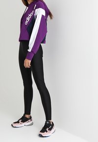 Felpa corta viola con accenti bianchi e blu navy, abbinata a leggings neri e sneakers multicolore con suola testurizzata.