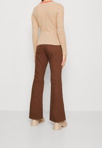 Gestreiftes langärmliges Oberteil in Beige und Rost, kombiniert mit braunen Schlaghosen und beigen klobigen Schuhen. Einfaches, figurbetontes Design mit Rückansicht.