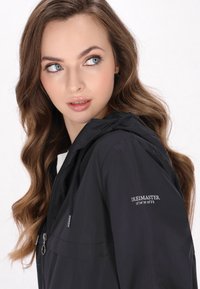 Giacca con cappuccio nera realizzata in tessuto leggero, dotata di zip frontale, coulisse regolabile e logo ricamato sulla manica.