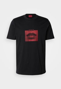 Zwarte katoenen t-shirt met een grafische print van rode lippen binnen een vierkant. De print heeft een stippenpatroon en toont het merk "HUGO" erboven.