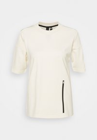 Krémové tričko s krátkým rukávem a kulatým výstřihem. Má černou kapsu se zipem na levé straně. Měkká, strukturovaná tkanina.