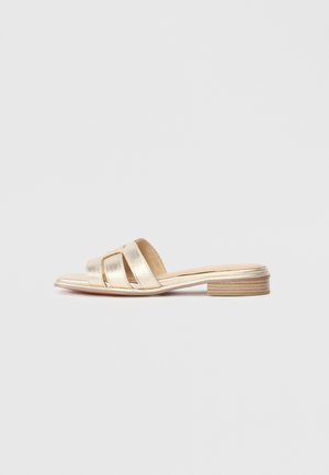 Sandale en or métallisé avec trois brides croisées et un talon en bois. Texture lisse avec une semelle plate. Design minimaliste.