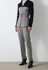 Traje de pata de gallo en blanco y negro que presenta un blazer estructurado con cinturón, combinado con pantalones ajustados y tacones negros de punta.