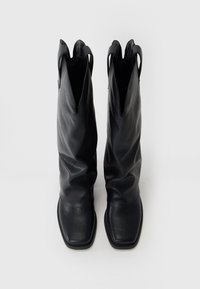 Paire de bottes hautes en cuir noir avec bouts carrés et languettes de tirage, vues de dessus sur un fond blanc uni.