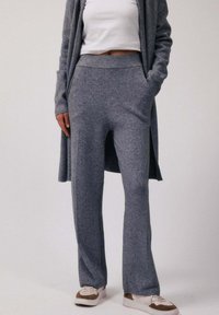 Personne portant un pantalon en maille gris et un cardigan assorti avec un crop top blanc et des baskets blanches avec des accents marron.