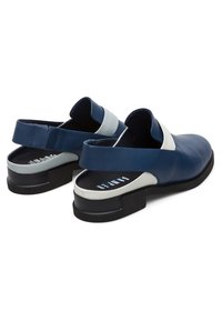 Chaussures à bride arrière en cuir bleu marine et blanc avec semelles noires, bouts arrondis et sangles réglables, visibles de dos et de côté.
