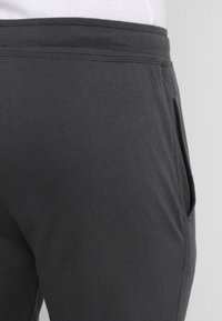 Grijze katoenen joggers met een gladde textuur, voorzien van een zijzak en een elastische tailleband. Focus op het eenvoudige, functionele ontwerp.
