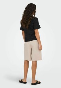 Schwarze Bluse mit Lochmuster und kurzen Ärmeln, kombiniert mit beigen maßgeschneiderten Shorts und schwarzen Rutschpantoletten, von hinten betrachtet.