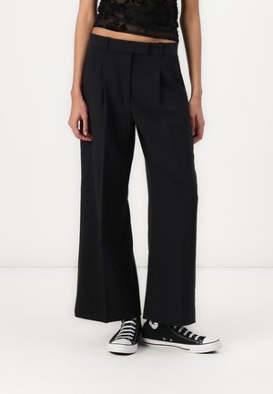 Svart vide bukser med en glatt tekstur, med belte midje og frontfold, stylet med svarte Converse-sko.