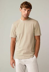 Beige T-Shirt mit kurzen Ärmeln aus Baumwolle, mit Rundhalsausschnitt, glatter Textur, normaler Schnitt, kombiniert mit hellen Hosen.