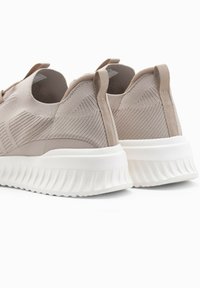 Sneaker beige in maglia con design testurizzato, parte superiore elasticizzata e suola in gomma bianca con accenti rigati. Inclusi tasselli posteriori per il trasporto.