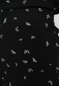 Tissu noir avec une finition texturée, présentant un motif de petits papillons blancs dispersés.