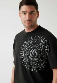 Zwarte katoenen t-shirt met een groot wit grafisch cirkels ontwerp met tekst en logo, korte mouwen en een klassieke ronde hals.
