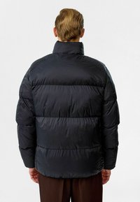 Doudoune en nylon noir avec un col montant, design matelassé et rembourrage épais. Présente une coupe décontractée et des poignets élastiques.