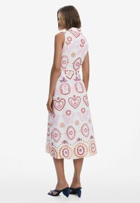 Weißes, ärmelloses Kleid mit bunten, gestickten Mustern in Rot, Rosa und Lila, das einen Kragen und ein fließendes, knielanges Design aufweist.