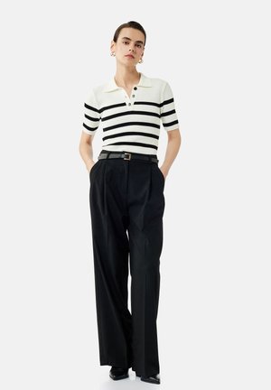 Gestreepte polo met korte mouwen in crème en zwart, met een kraag en drie knopen. Hoge taille zwarte broek met een riem.