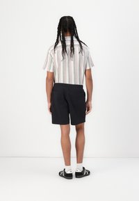 Kortermet stripet skjorte med pastellfarger, paret med svarte shorts med elastisk midje og baklommer, brukt med svarte sko.