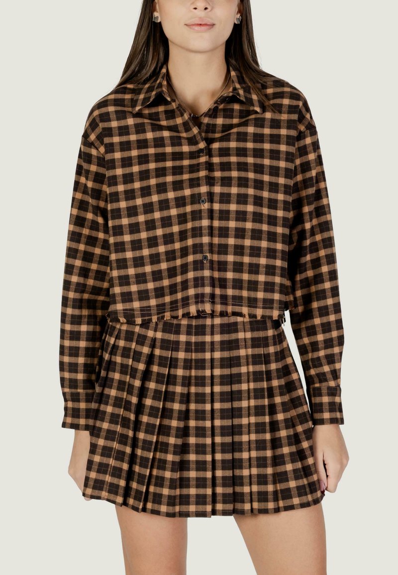 Top corto a quadri marrone e beige con design a bottoni, abbinato a una gonna plissettata. Il tessuto appare morbido con uno stile informale.