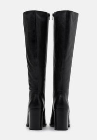 Bottes noires montantes en cuir lisse. Elles présentent un talon carré et une fermeture éclair à l'arrière. Lignes épurées avec un design élégant.