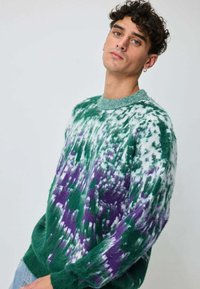 Pull tie-dye vert et violet avec une texture duveteuse, col côtelé et manches longues. Présente une coupe ample et un motif superposé.