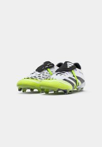 Încălțări de fotbal cu un design alb și negru, având accente verde neon, un suprafață texturată și mai multe cuie pe talpă pentru aderență.