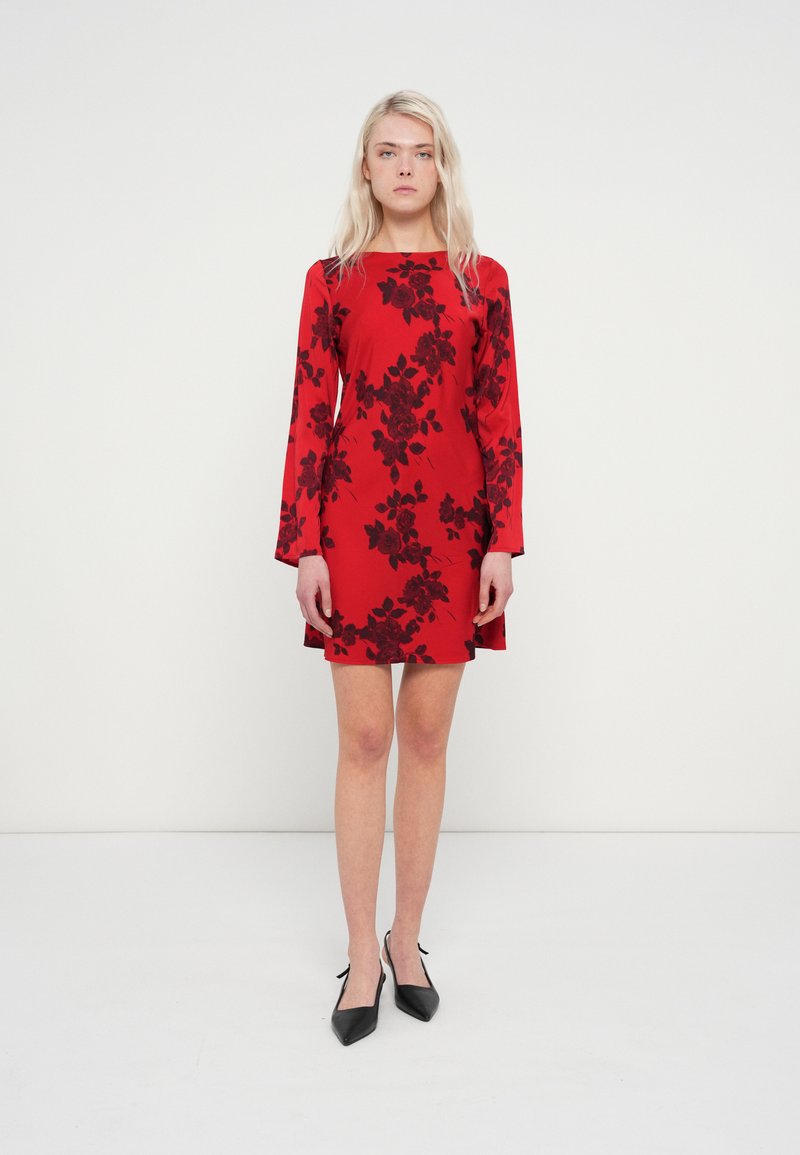 Crvena haljina s dugim rukavima ukrašena crnim cvjetnim uzorkom. Izrađena od glatkog tkanja, ima opušteni kroj i ravnu donju ivicu.