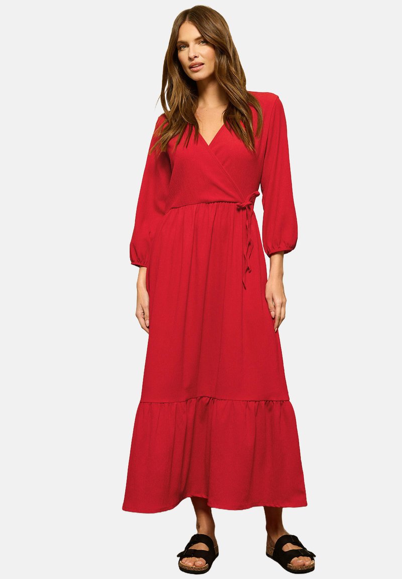 Vestido rojo de manga larga, con falda en capas y un lazo en la cintura. Hecho de una tela ligera, presenta una textura suave.