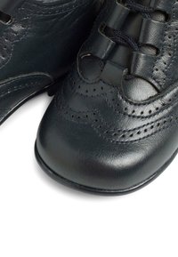 Scarpe in pelle nera con punta rotonda, caratterizzate da cuciture intricate, dettagli perforati e lacci neri, su sfondo bianco.