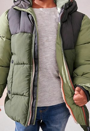 Gefütterte Jacke mit Kapuze in einem dunkelgrünen und grauen Farbschema, mit Reißverschluss und Knopf-Akzenten. Getragen über einem grauen Shirt.