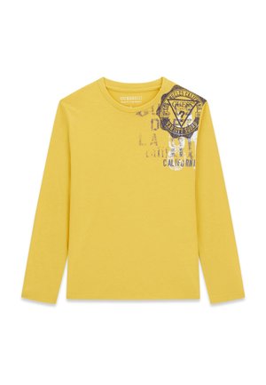 Chemise jaune à manches longues avec col rond, avec un imprimé fané noir et blanc style varsity et du texte sur la partie supérieure gauche de la poitrine.
