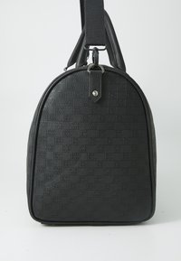 Borsa nera con texture, dalla forma arrotondata, caratterizzata da una superficie decorata e una tracolla removibile. Dotata di accessori sulla parte superiore.