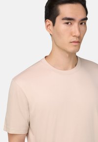 Gai bēšas krāsas T-krekls ar apaļu kakla izgriezumu un īsām piedurknēm, izgatavots no gludas auduma. Vienkāršs dizains bez redzamām rakstām vai grafikām.