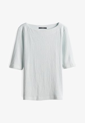 Haut bleu clair texturé avec un large col et des manches courtes. Le tissu présente un motif subtil et irrégulier dans l'ensemble.