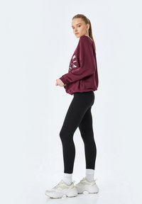 Bordeaux sweatshirt met witte grafische print, zwarte leggings en lichte sneakers. De outfit heeft een relaxte pasvorm en een gladde stof.