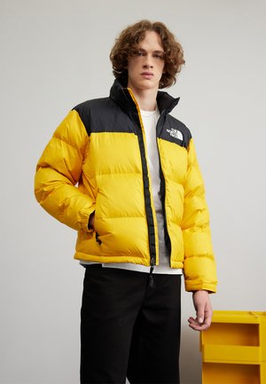 Doudoune avec un design bicolore jaune et noir, fabriquée en matériau brillant. Présente un col haut, une fermeture éclair et des poignets élastiques.