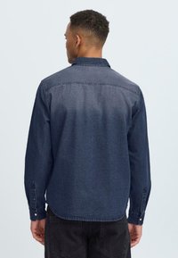 Donker denim overhemd met lange mouwen, een kraag en enkele knoopmanchetten, met een vervaagde textuur en subtiele stikseldetails.