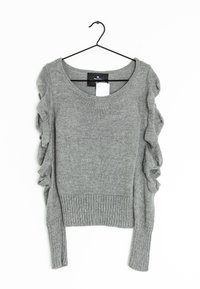 Grå strikket sweater med ribbestrikket kant og lange ærmer, der har bølgede detaljer langs skuldrene. Hænger på en sort krog.