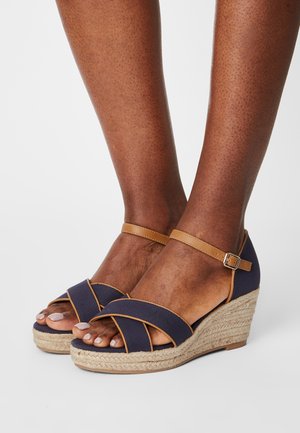 Marine wedgesandal med kryssremdesign, beige ankelrem og jutewrapt kilehel. Den har en teksturert overdel i stoff og åpen tå.