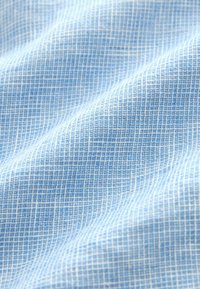 Tissu bleu clair avec un motif à carreaux blanc, présenté en gros plan avec des plis doux et une texture tissée visible.