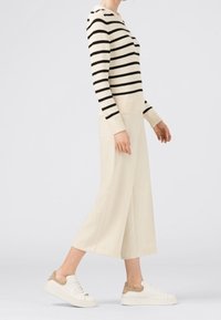 Sweter w paski z dzianiny w kolorze kremowym i czarnym, kremowe spodnie z szerokimi nogawkami oraz białe trampki z beżowymi akcentami, prezentujące swobodny, casualowy styl.